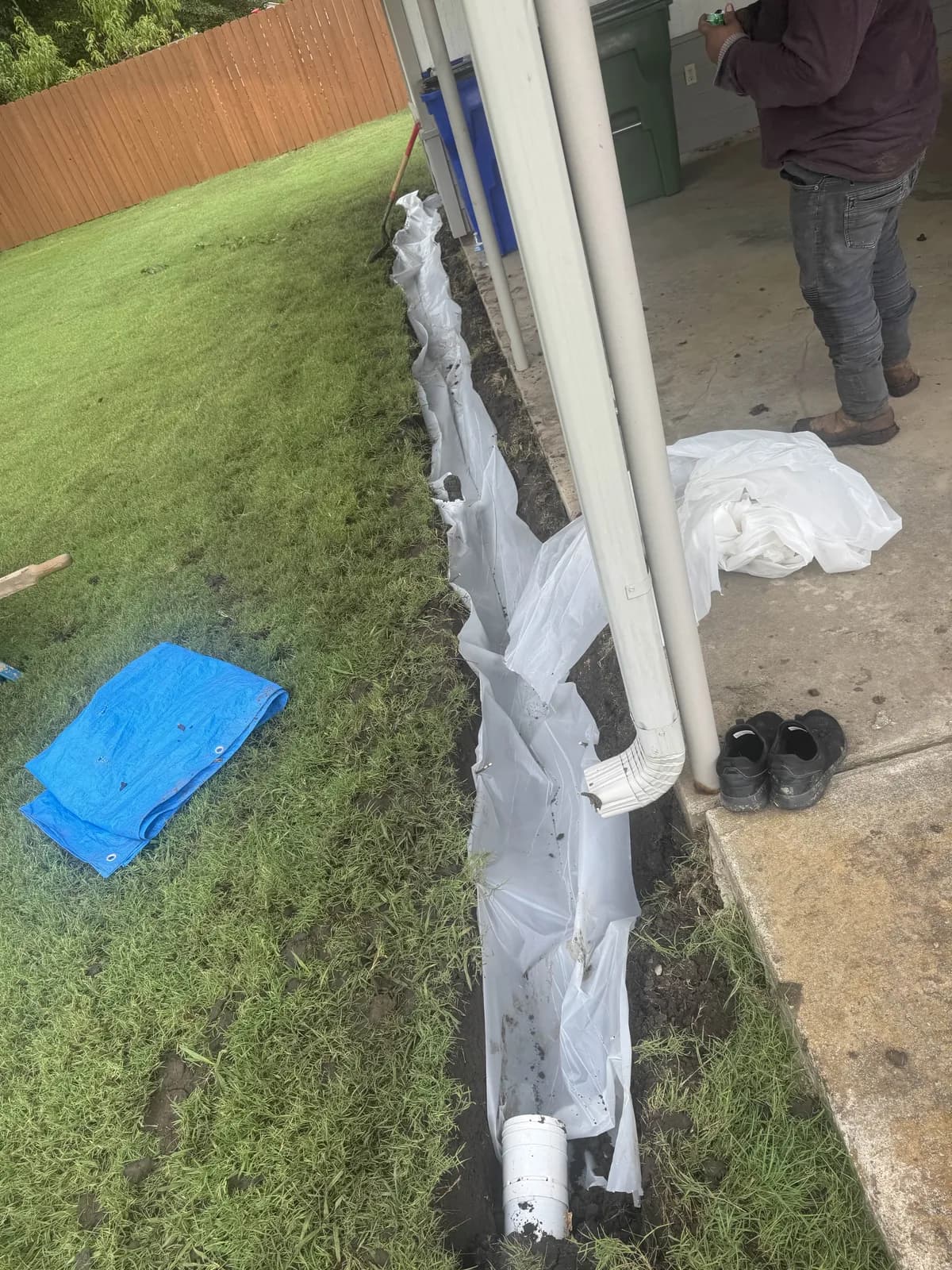 Open trench lined with filter fabric along the side of a house during French drain installation