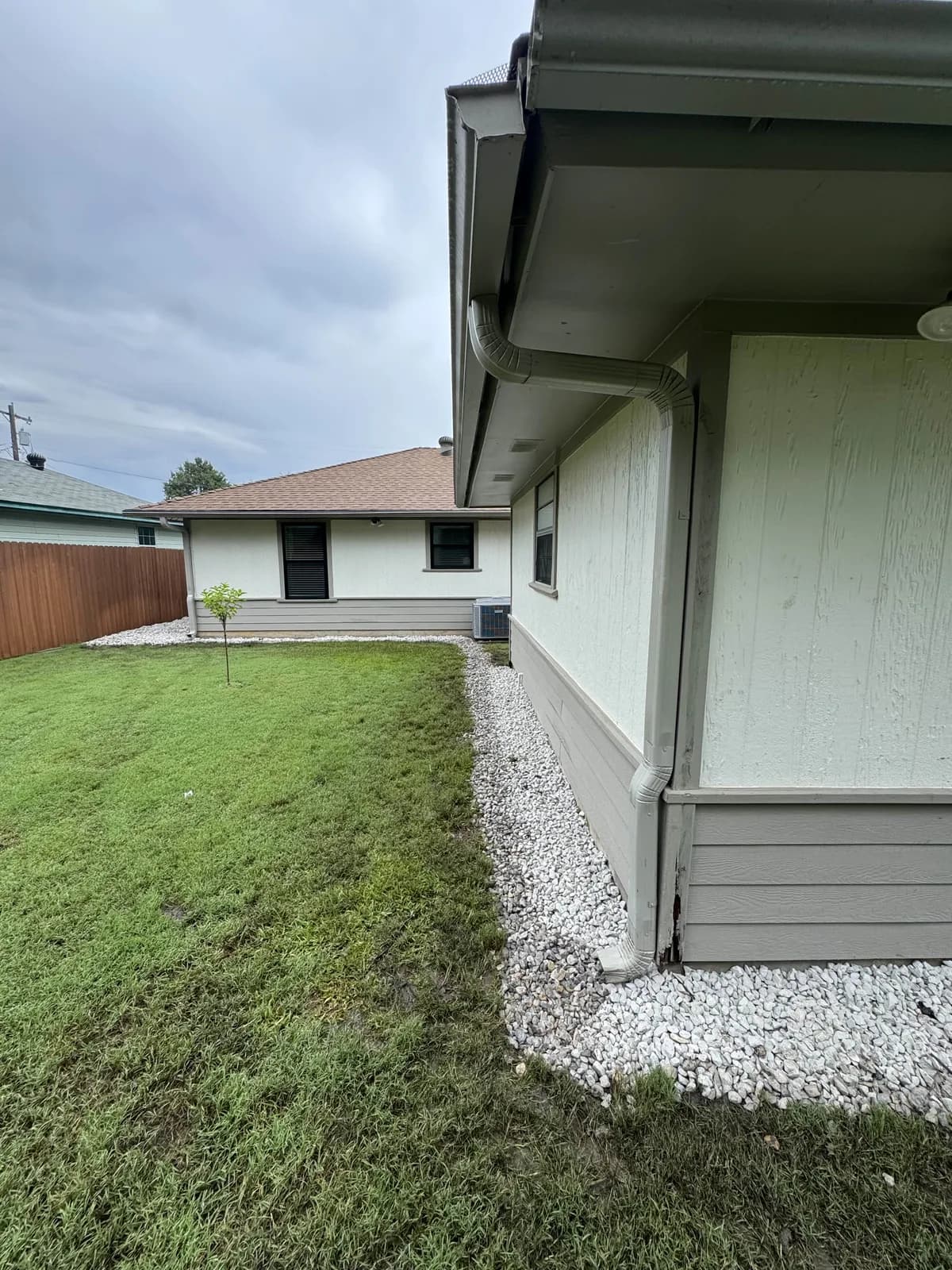 Finished French drain with white gravel along the corner of a house and fresh sod
