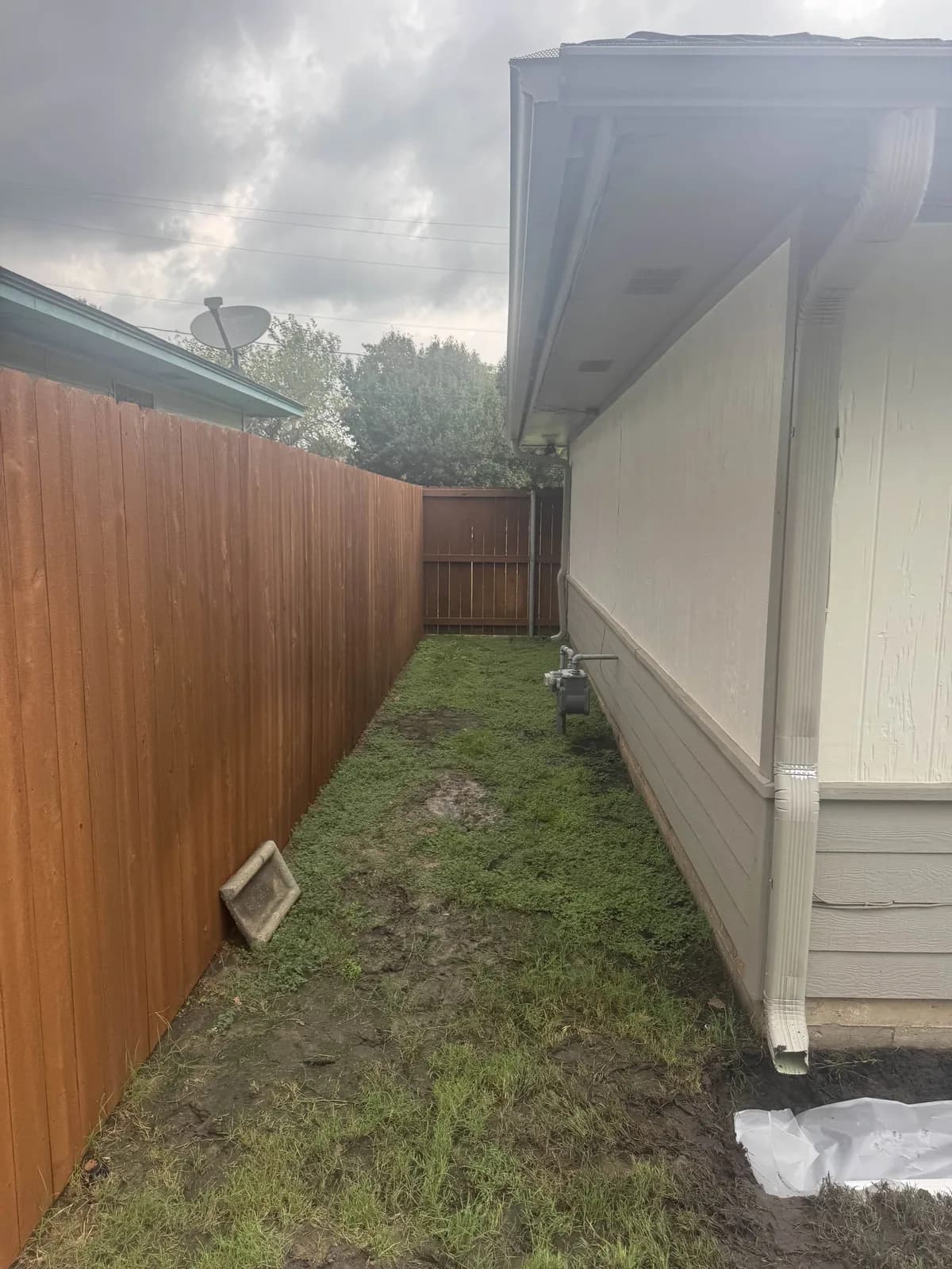 Gravel filled French drain running along the foundation of a white house beside a wood fence